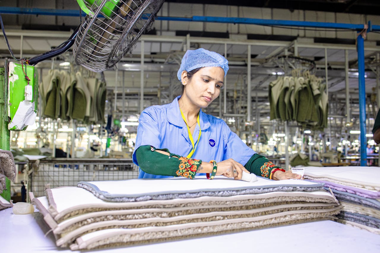 Female textile worker in a factory inspecting fabric layers under bright lighting.